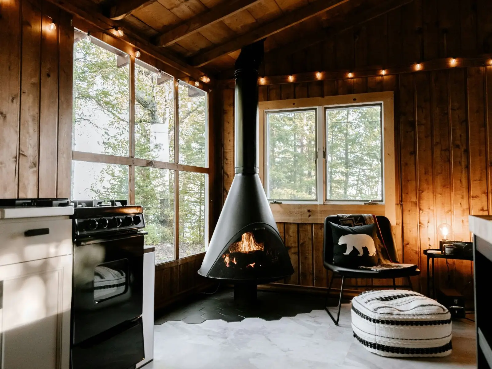 A cabin interior with a hanging fireplace and string lights