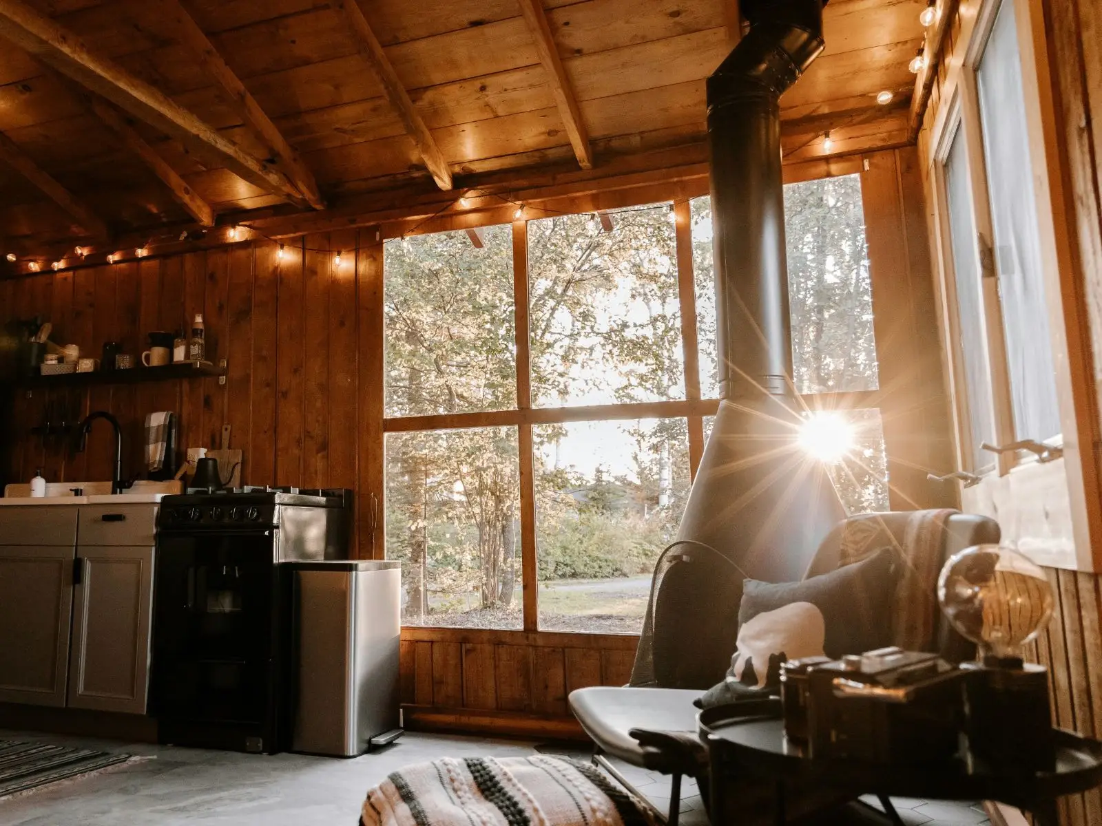 A cabin interior with a hanging fireplace and the sun through the windows