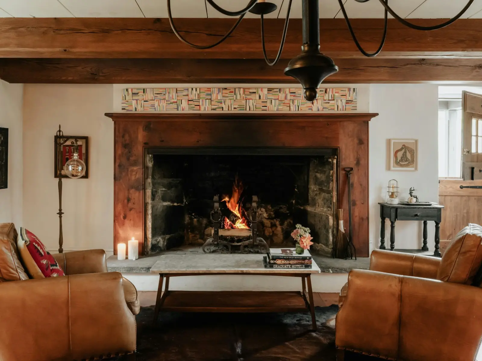 A stone fireplace with a lit fire between two leather armchairs