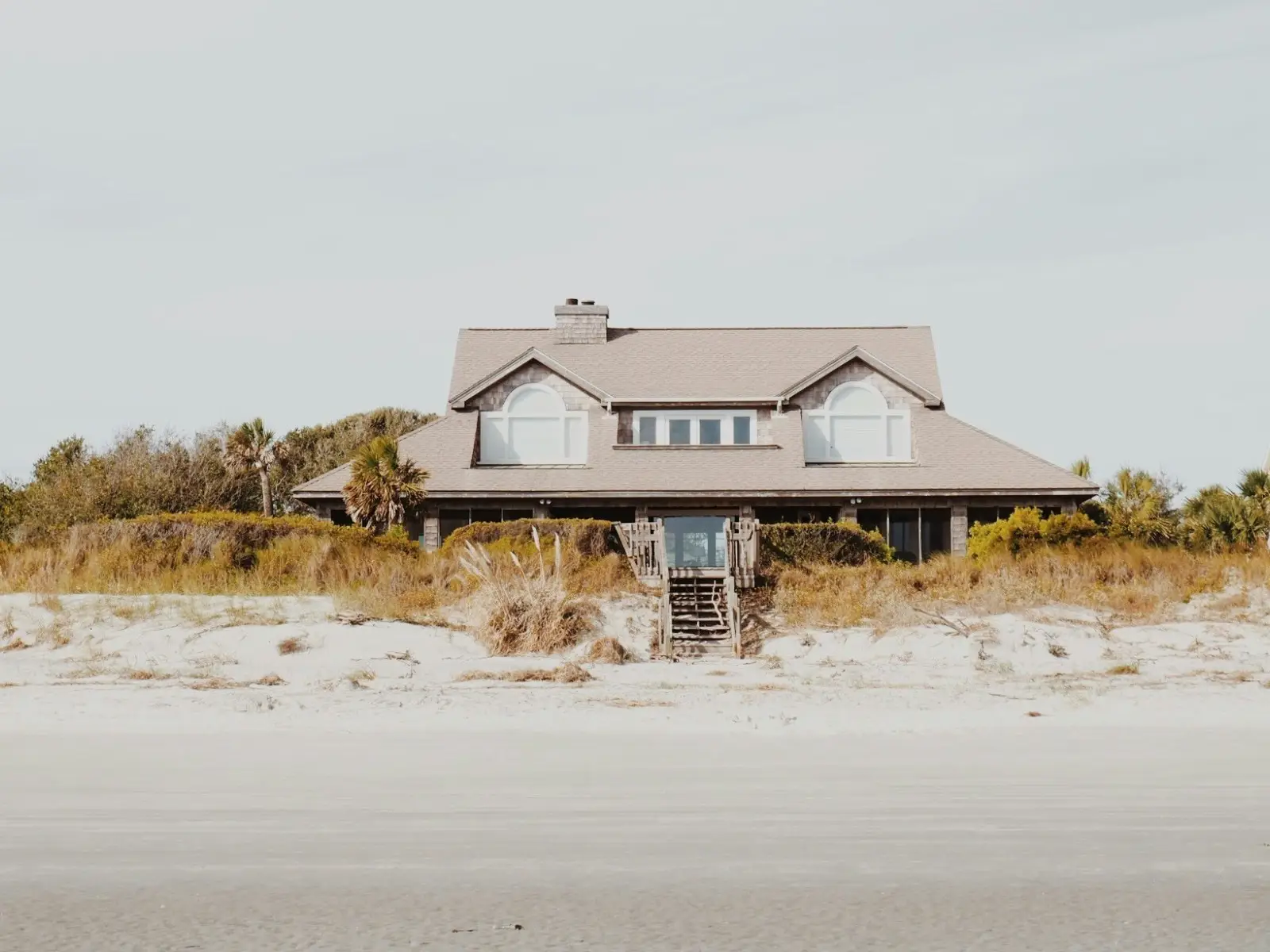 A shingled beach house behind dunes and sea oats