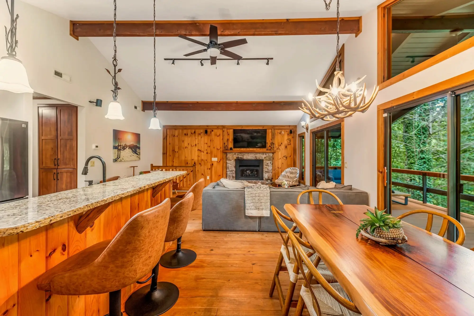 Open kitchen, dining table and living room with a stone fireplace and wood-paneled walls